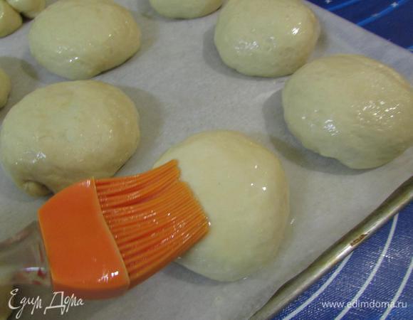 Противень застелить бумагой для выпечки, обязательно смазать сливочным маслом. Выложить подготовленные булочки швом вниз. И смазать их яйцом. 