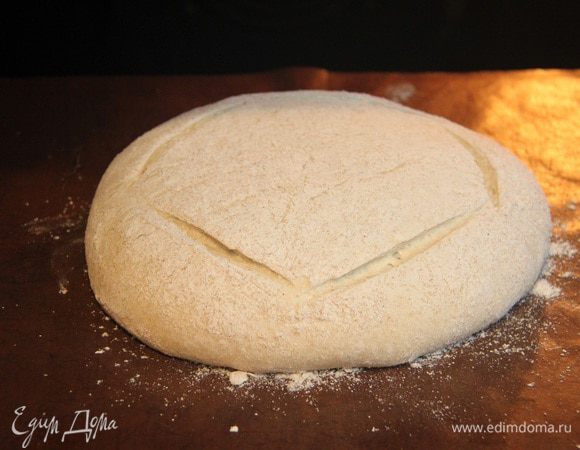 Через час тесто обмять, оставить на расстойку на 1 час. Через указанное время тесто выложить на рабочий стол, придать форму шара, обвалять со всех сторон ц/з мукой. Оставить под полотенцем на 1 час. Духовку разогреть до 250°С вместе с противнем. Хлеб выложить на горячий противень, быстрыми движениями сделать надрезы ножом. Выпекать 10 минут при 250°С с паром, затем 25 — 30 минут при 180°С без пара.
