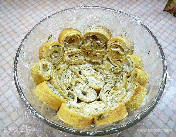 Круглый салатник выстилаем пищевой пленкой, чтобы свисали края. Выкладываем блинные рулетики сначала на дно, потом по бокам.