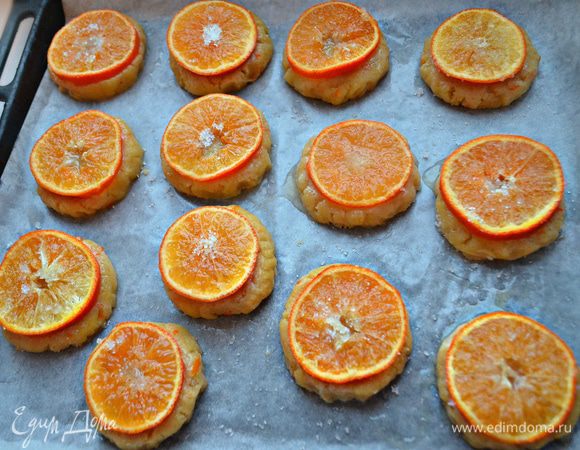 Противень застелите пекарской бумагой и слегка смажьте сливочным маслом. Выложите заготовки на противень, сверху присыпьте сахаром, сверху смажьте белком, выложите кружки мандаринов, слегка прижимая к тесту, и снова присыпьте сахаром. Выпекайте печенье в разогретой духовке до 200°С 20 — 25 мин. 