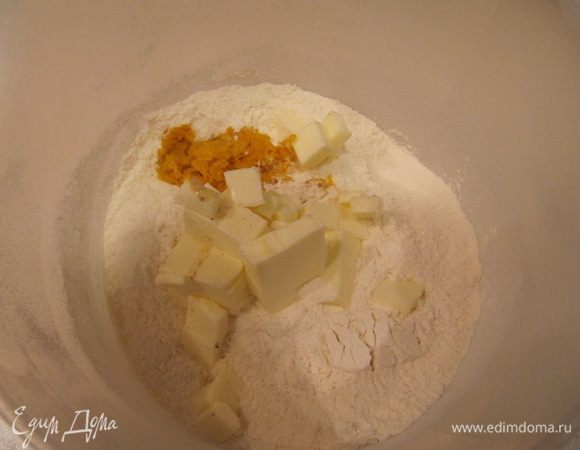 Просеянную муку перемешать с сахаром, разрыхлителем, содой, солью и цедрой апельсина. Добавить порезанное на кусочки холодное сливочное масло.