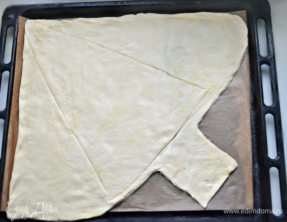 Слоеное дрожжевое тесто разморозьте. Противень для запекания застелите пекарской бумагой и смажьте немного растительным маслом. Тесто раскатайте по величине противня и выложите на пекарскую бумагу. Срежьте снизу лишнее тесто, формируя ствол елки. Тупой стороной ножа или шпажкой обозначьте контур елки.