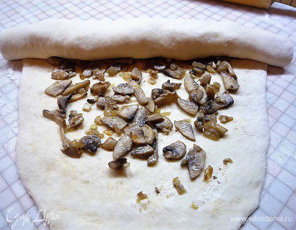 Раскатываем тесто в пласт, распределяем начинку из грибов, оставляя свободные края примерно 4 см и сворачиваем в толстый рулет.