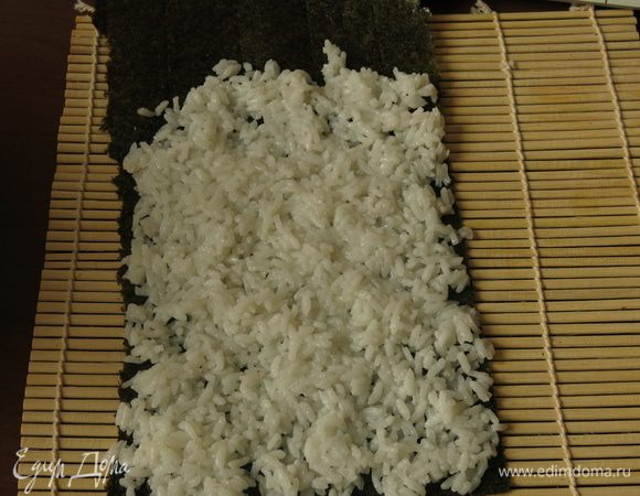 Выкладываем рис на нори так, чтобы обхватить по кругу рулет из омлета.