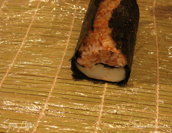 Поднимаем листы нори от края к центру, так, чтобы сохранить положение цветного риса над кальмаром, внутри получается фигура овал.