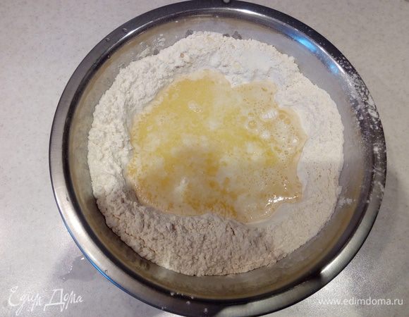 Сливочное масло растопить и остудить. 
Сделать в центре мучной смеси углубление и влить в него растопленное масло, теплую воду (не горячую!), 1 яйцо и 1 яичный белок. Желток оставьте для смазки пирога.