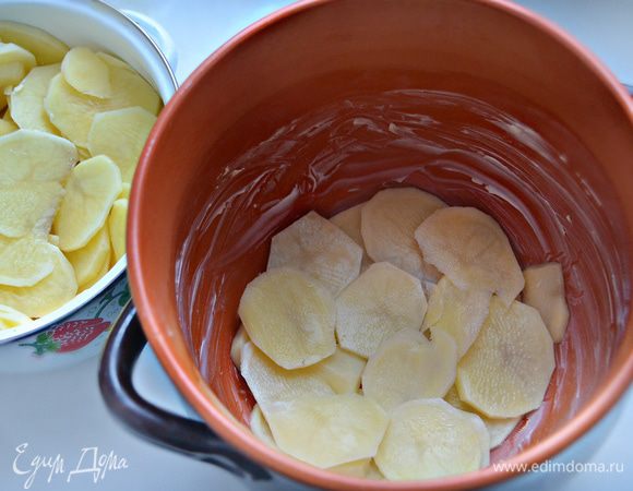 Дно и стенки керамической формы (горшочка) смажьте сливочным маслом, уложите часть картофеля.