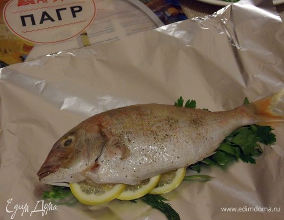 Выкладываем на смазанную растительным маслом фольгу петрушку и укроп, сверху кладем рыбу. Брюшко пагра заполняем дольками лимона и заворачиваем фольгу.
