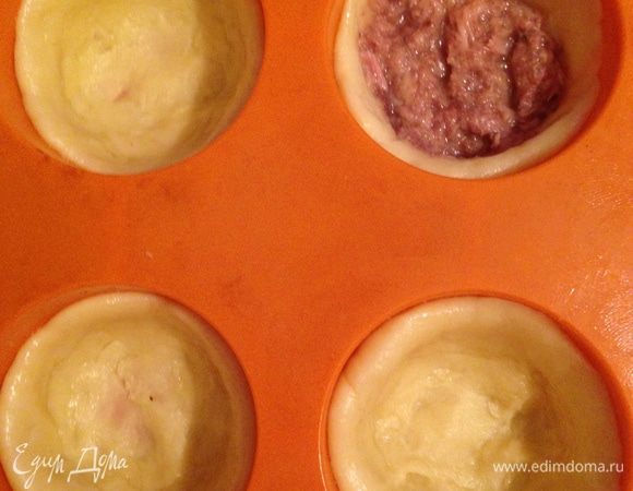 Тесто разделить на небольшие шарики. Из каждого шарика сформовать лепешку и поместить в форму, сформировав бортики. Консервированного тунца размять вилкой в кашицу. На дно каждой лепешки положить по 1 ч. л. тунца.