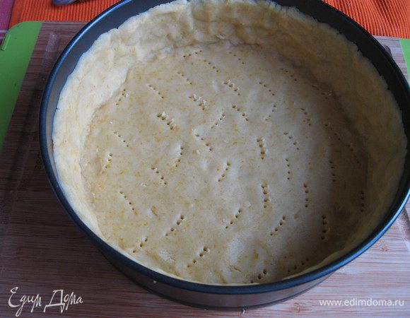 Песочное тесто раскатать на рабочей поверхности, накрытой кружком пекарской бумаги размером с донышко формы. Подставить под тесто и бумагу донышко формы и перенести вместе с донышком к бортикам формы. Закрыть бортики, сформировав ровные борта из теста, бортики из теста должны быть максимально высокие. Наколоть тесто вилкой, убрать форму на 5 — 10 минут в холодильник. 
