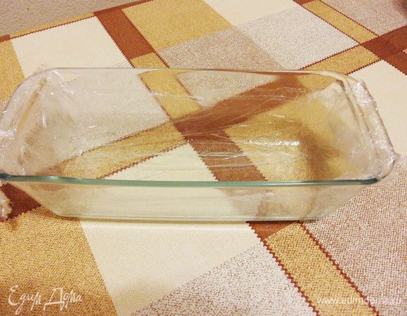 Подготовить прямоугольную форму. Смазать ее тонким слоем сливочного масла, чтобы прилипла пленка, выстелить пищевой пленкой. Выстеленную пленку также немного смазать маслом, чтобы легко отделился готовый десерт.