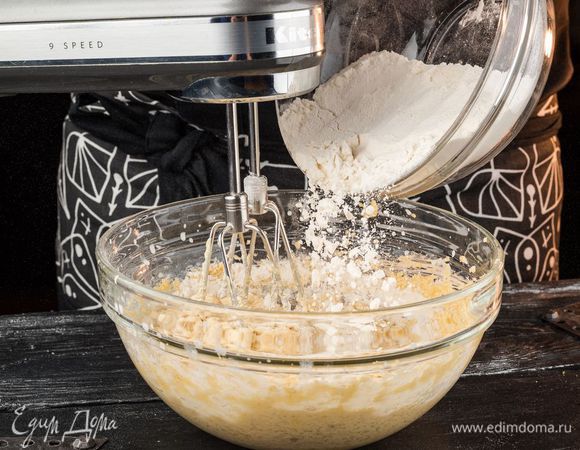 Продолжая вымешивать, небольшими порциями ввести половину муки.