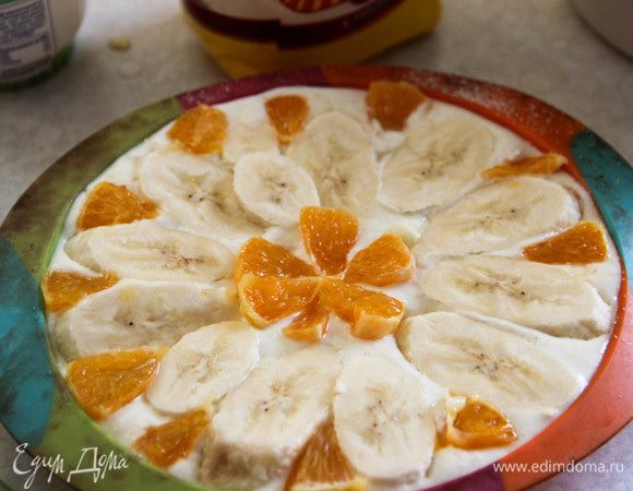 Форму для выпечки смазываем растительным маслом, присыпаем манкой. Выливаем творожно-банановую массу. Сверху раскладываем кружочки банана и нарезанные произвольно кусочки апельсина. Слегка притапливаем фрукты в смеси. Выпекаем при температуре 180°С минут 40.