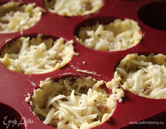 В форму для маффинoв укладываем ст. ложку «теста», выкладывая дно и стенки, формируем стаканчик. В него кладем грибы, немного тертого сыра.