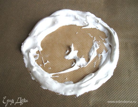 Начать выкладывать большой ложкой взбитые белки по периметру круга. Подложенную под пекарскую бумагу белую бумагу убрать.