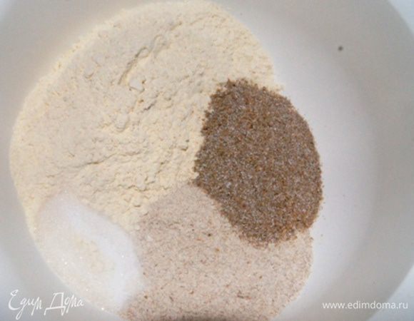 Смешать оба вида муки, отруби, сахар и соль. Добавить оставшиеся 200 мл теплой воды и дрожжи.
