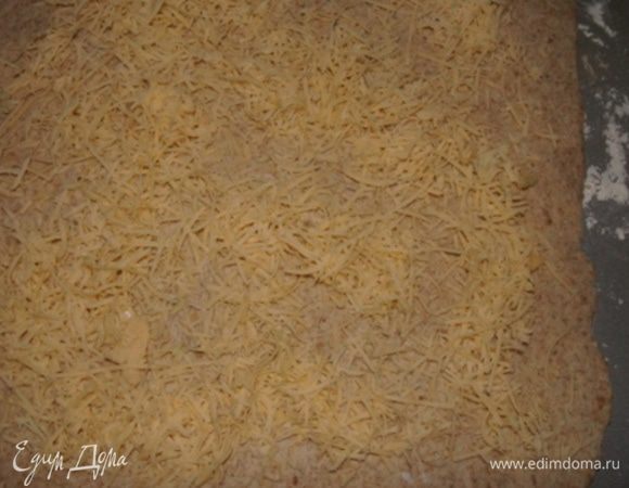 Тесто обмять. Стол присыпать мукой и раскатать тесто в пласт. Присыпать тертым сыром и измельченным чесноком.