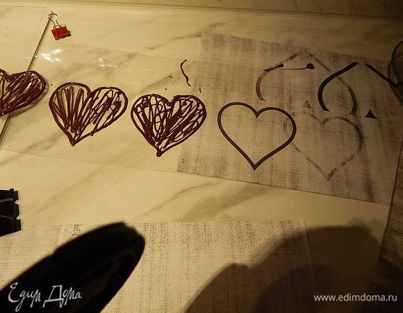 Ацетатную пленку или пергамент положить поверх рисунка. Теперь осторожно выдавить шоколад по контуру рисунка. Затем внутри контура произвольно нанести рисунок.