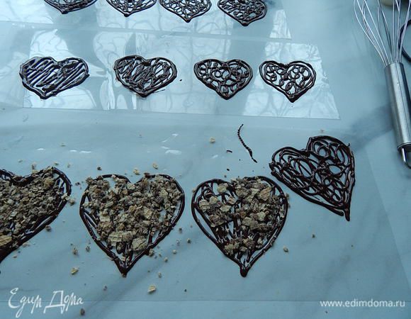 Пока еще шоколад не затвердел, сверху посыпать на одни сердечки обжаренные орехи, на другие раскрошить вафли, на следующие посыпать кофе, можно слегка придавить посыпку на шоколад. Оставшийся шоколад полить сверху посыпки. Оставить шоколадные заготовки хорошо затвердеть при комнатной температуре, на это уйдет примерно 25 — 35 минут.