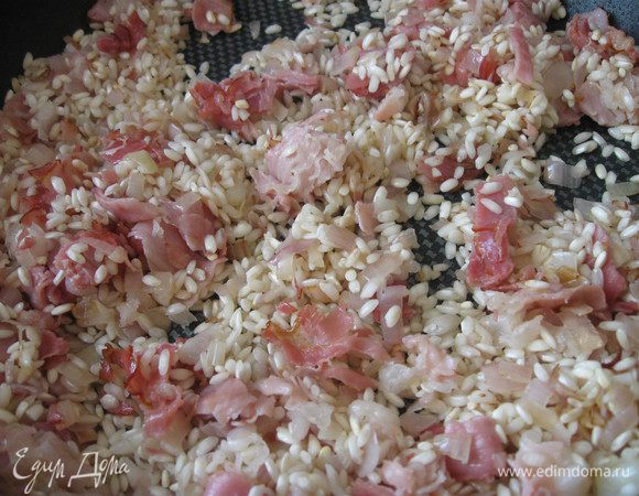 Отлить 200 мл от общего количества хорошего домашнего куриного бульона в отдельную кастрюльку, он вам может понадобиться в самом конце процесса. Остальной (1,5 литра) довести  до кипения в отдельной кастрюле, убавить огонь и так держать бульон на медленном огне в течение всего приготовления блюда. В сковороду с луком и беконом (панчеттой) добавить рис для ризотто и обжаривать его в течение 3 — 4 минут, чуть увеличив температуру. 
