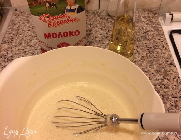 Молоко «Домик в деревне» довести до кипения и влить тонкой струйкой в тесто, непрерывно взбивая венчиком. Затем добавить растительное масло и еще раз хорошо взбить.