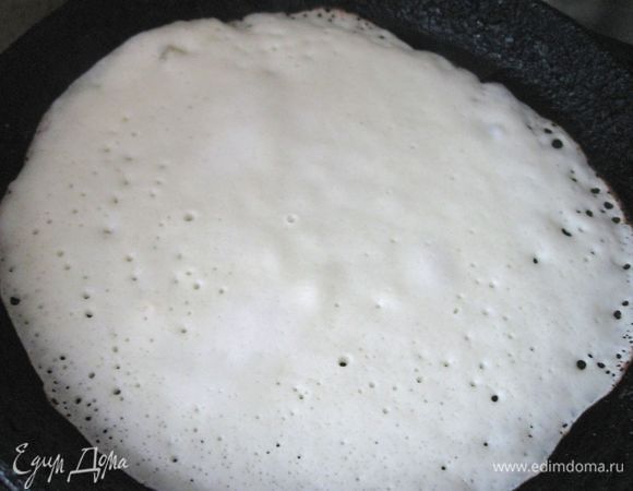 На огонь поставить кастрюлю с налитой в нее водой (примерно 1/3 часть кастрюли), дать закипеть, убавить огонь до минимального, на кастрюлю поставить миску, в которую будете складывать готовые блины. Они во время всей готовки будут находиться на паровой бане на медленном огне.  Держите под рукой сливочное масло, которым периодически будете смазывать блины в миске.
Раскалить чугунную сковородку для блинов на сильном огне, убавить огонь до средне-сильного. В блюдечко налить оливковое масло, наколоть на вилку половинку очищенной картофелины или репчатого лука, смазать маслом сковороду (так смазывали блинные сковороды еще наши бабушки: масла на сковороде будет именно столько, сколько нужно, и распределяется оно равномерно, это предпочтительнее использования силиконовой кисточки). Половником налить на сковородку тесто, немного наклоняя сковородку, чтобы тесто распределилось равномерно.Через некоторое время перевернуть блин ножом с длинным лезвием и закругленным концом. Снять блин со сковороды и поместить в миску.
