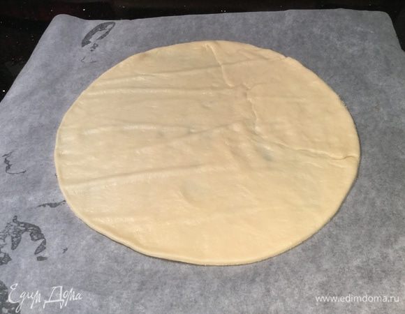 Тесто разделите на две части. Смажьте рабочую поверхность растительным маслом и раскатайте половину теста, вырежьте круг диаметром 28 — 30 см, с помощью скалки переложите его на противень, застеленный бумагой для выпечки.