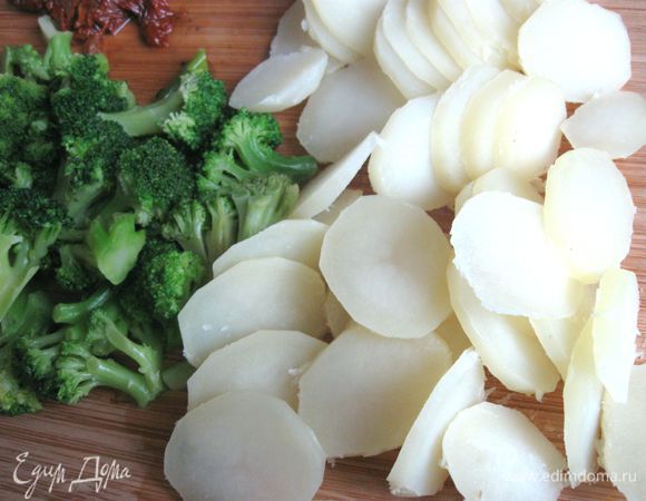 Картофель порезать на тонкие кружочки. Замороженную брокколи бланшировать в отдельной кастрюле 2 — 3 минуты. Воду слить, дать просохнуть брокколи и остыть. Вяленые в масле томаты порезать.