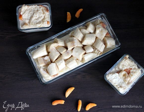 Форму выстилаем слоем булки, заливаем кремом. Сверху кладем курагу и слой бананов. Закрываем блюдо сдобой, заливаем остатками жидкости и слегка придавливаем. Желательно, чтобы содержимое было почти до верху покрыто заливкой. Не скупясь присыпаем сахарной пудрой.