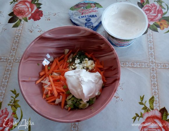 В чашку выкладываем нарезанные овощи, чеснок и зелень. Добавляем 1 ст. л. сметаны. Солим.