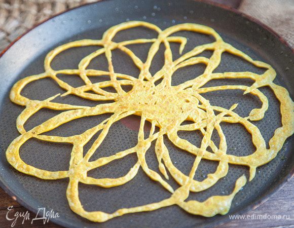 На среднем огне разогрейте растительное масло, а затем, словно рисуя тестом, добавьте на сковороду порцию теста.
Наиболее традиционным считается рисунок, напоминающий кружево. На деле рисунок может быть произвольным, главное, чтобы линии были цельными, а центр — чуть более плотным, чем края. Я обычно рисую «цветочек» со множеством лепестков.