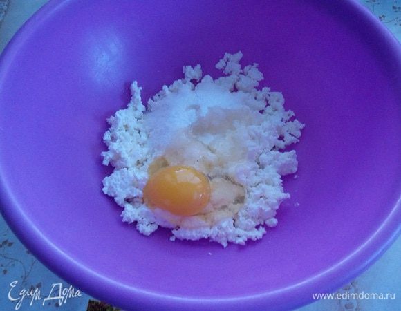 В чашку выкладываем творог «Домик в деревне». Хорошо разминаем вилкой. Добавляем щепотку соли, сахар и взбитое яйцо. Хорошо перемешиваем.