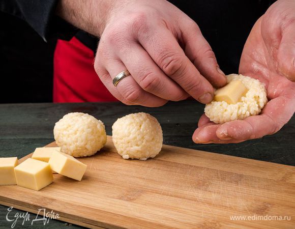 Из рисовой массы влажными руками сформировать шарики, поместив внутрь каждого квадратик мягкого сыра.