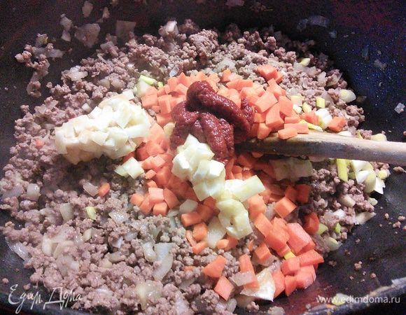 Добавить сельдерей (у меня кусочек корневого сельдерея) и морковь, томатную пасту и еще несколько минут обжарить вместе с мясом. 