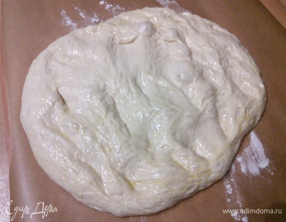 Рабочую поверхность щедро припылить мукой. С помощью лопаточки дать тесту сползти из миски на поверхность. Аккуратно пальчиками растянуть тесто, чтобы получить прямоугольник и разрезать на 2 равные части. Аккуратно переложить каждую фокаччу на отдельный лист пергамента, опять руками осторожно растянуть в прямоугольник, следить за тем, чтобы не повредить пузырьки воздуха. 