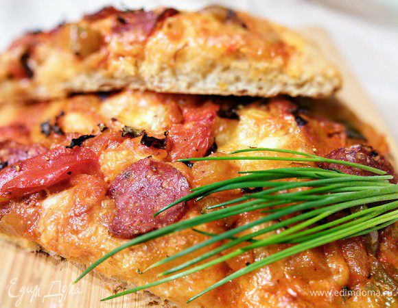 Достать горячий противень, выложить на него пергамент с фокаччей, выпекать на нижнем ярусе духовки 10 мин, затем переместить противень в середину духовки, уменьшить температуру до 200°С и печь еще 10 минут. Этот метод имитирует выпечку на камне, именно из-за этого дно фокаччи так аппетитно хрустит. 