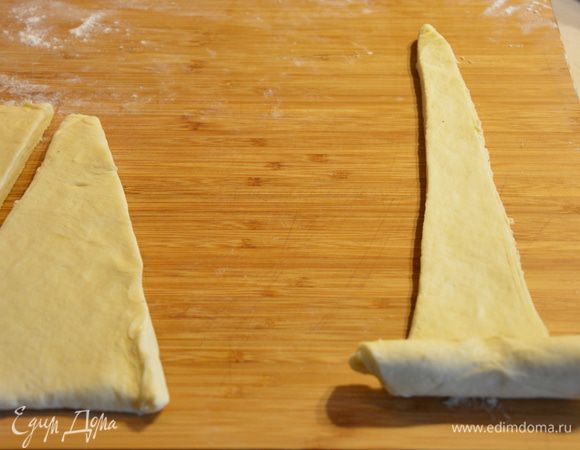 Формируем круассан: заворачиваем длинный край от себя до конца, немного вытягивая тесто в длину.