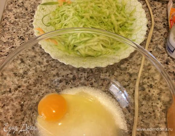 Духовку нагреть до 180°С Форму (у меня 20х26) застелить бумагой для выпечки. Цукини натереть на крупной терке. Яйцо взбить с сахаром и ванильным сахаром.