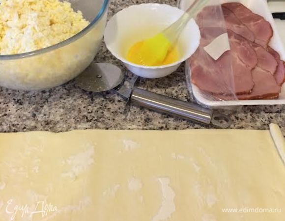 Духовку нагреть до 190°С. Сыр натереть на крупной терке, добавить белок и хорошо перемешать. Желток смешать с молоком. Слоеное тесто разделить на три части.