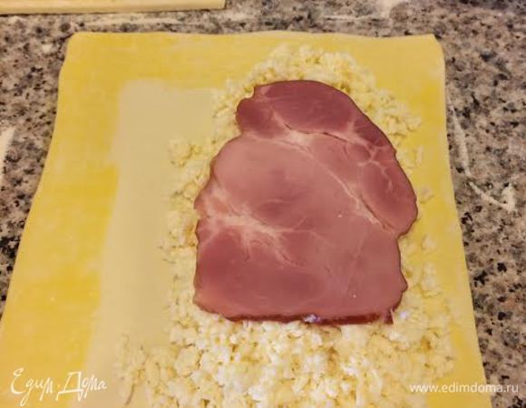 Каждую часть слегка раскатать, края смазать желтком с молоком, выложить сыр на половину теста, сверху положить ветчину.
