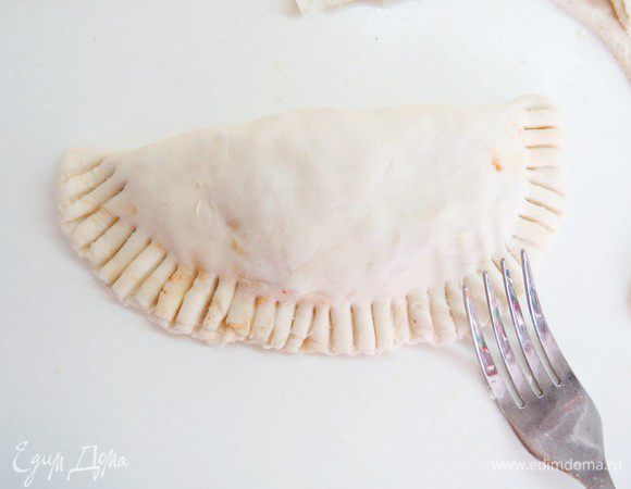 Смачиваем немного водой края и защипываем их, хорошо прижимая пальцами или вилкой.  Взбиваем вилкой 1 яичный желток и смазываем им наши пирожки. Печь в разогретой до 180°С духовке в течение 25-30 минут.