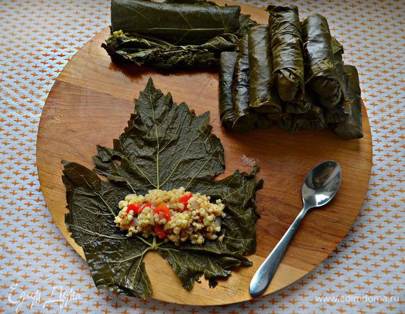 Виноградные листья разложите на ровной поверхности. На внутреннюю сторону каждого листа положите начинку и заверните трубочкой, по принципу формирования голубцов.