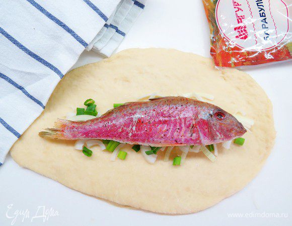 Тесто раскатываем в довольно тонкий пласт, на тесто выкладываем лук и часть зеленого лука. Сверху кладем нашу рыбку. 