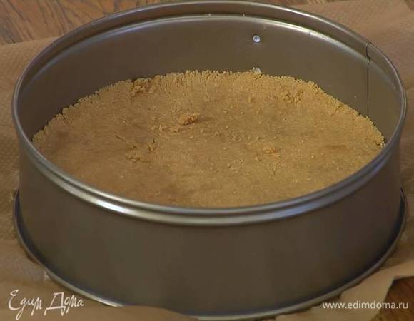 Дно разъемной формы выстелить бумагой для выпечки, равномерно выложить измельченное печенье с маслом и уплотнить ложкой, так чтобы получился корж толщиной в 1 см.