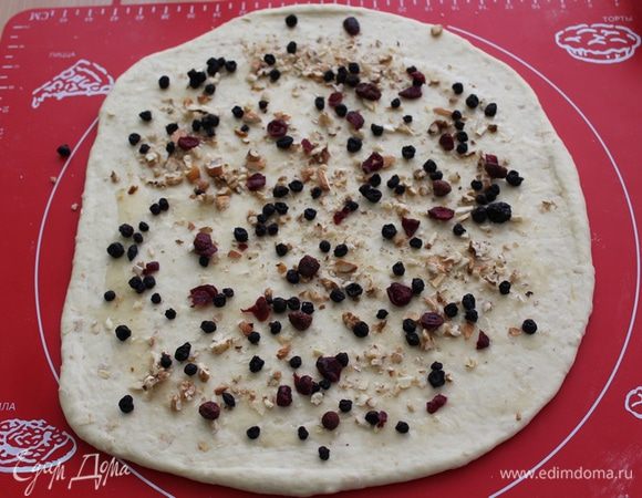 Тесто раскатываем толщиной где-то 2,5 миллиметра, смазываем медом. Равномерно распределяем ягоды, орехи. 