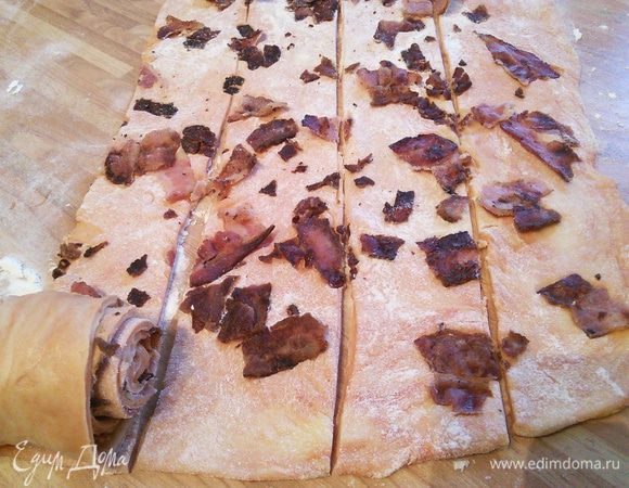 Через это время можно продолжить работу с тестом. Раскатать томатное, посыпать кусочками бекона, пройтись скалкой, чтобы бекон оставался на своем месте, разрезать на равные полоски. 