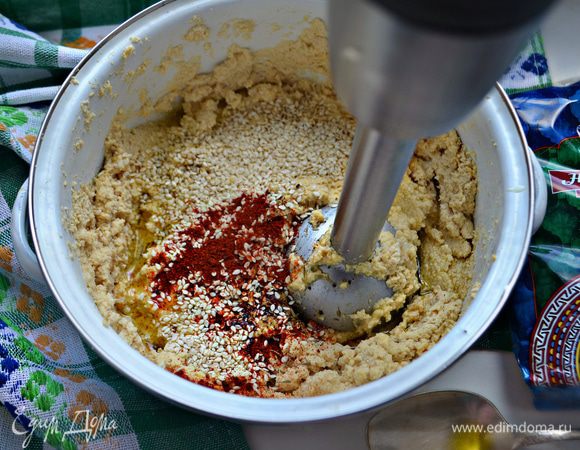 К нуту добавьте чеснок и взбивайте с помощью блендера, периодически добавляя лимонный сок. При необходимости добавьте 1-2 ст. л. кипяченой воды.  Далее в нутовую массу добавьте соль, паприку, перец, кунжут, тмин и оливковое масло. Взбить блендером.