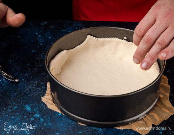 Выложите в форму слоеное тесто, наколите вилкой в нескольких местах. Бортики необходимо оставить высокими, чтобы начинка не вытекла. Разогрейте духовку до 180°С.