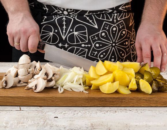 Картофель отварить в «мундире», очистить и нарезать крупными кубиками. Маринованные грибы помыть, откинуть на дуршлаг и нарезать. Соленые огурцы нарезать кубиками. Лук нарезать соломкой. Измельчить зелень.