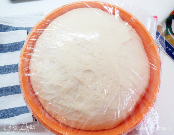 Через полчаса выложить заметно поднявшееся тесто на стол и еще раз обмять. Опять скатать в шар, положить в миску и затянуть пленкой. Оставить тесто еще на 40 минут до окончательного подъема.